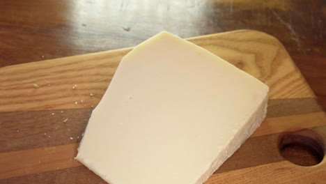 wedge of old hard cheddar cheese is cut with cheese knife on board