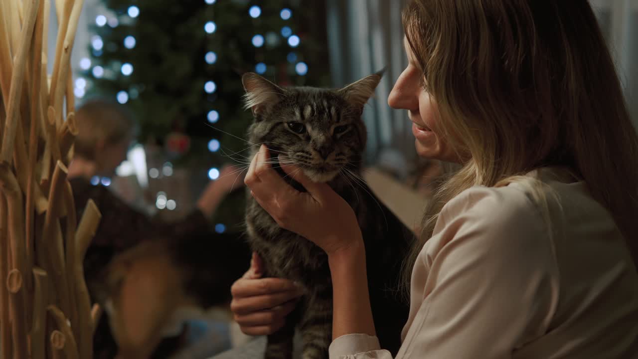 мама ласкает красивую кошку. на заднем плане дети играют с собакой под деревом.