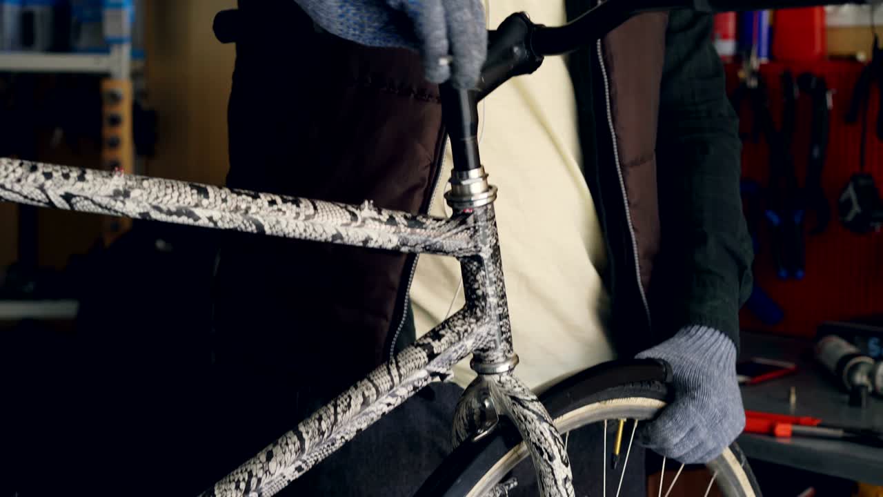 젊은 남성의 트 다운, 이어폰을 착용한 전문 수리공이 앨런 키를 사용하여 자전거 니바를 고정하고 보호 장갑을 입은 손으로 스티어링 을 들고 있습니다.