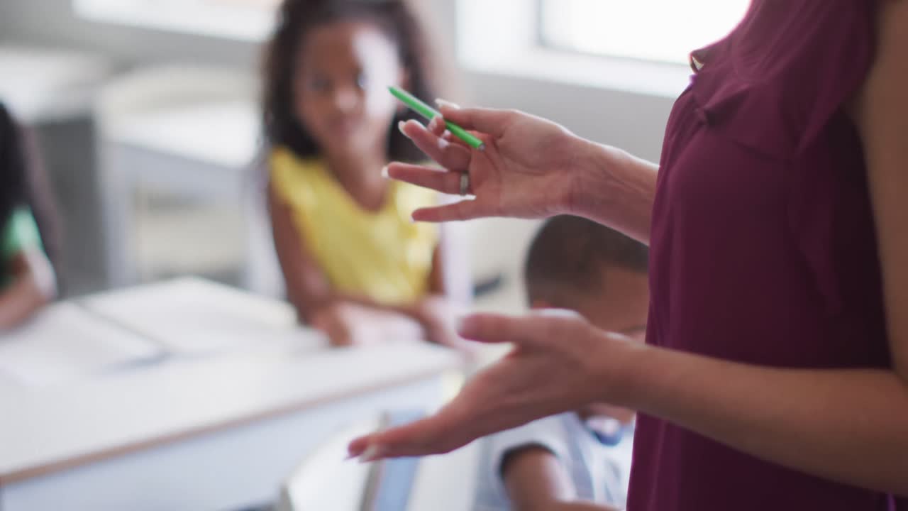 video de la sección media de una maestra de escuela caucásica que estudia a niños diversos en el aula
