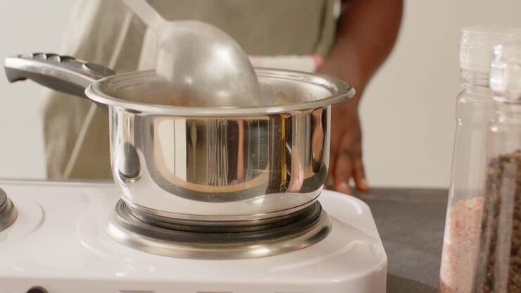 Man reaching for ladle and stirring simmering saucepan on electric hot plate, preparing meal