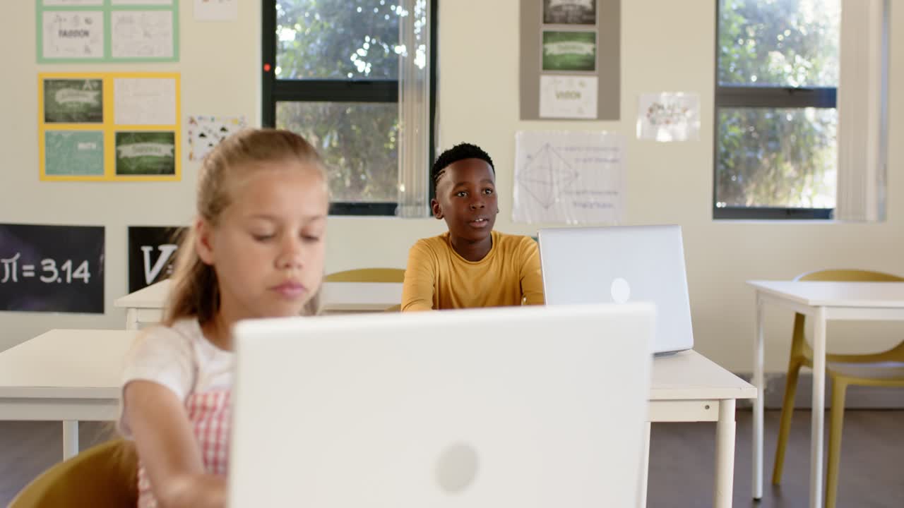 Diverse teenage classmates, boy responding to prompt, calling as girl typing on laptop in classroom