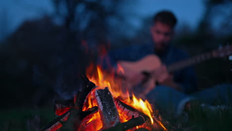 man playing guitar near bonfire. lonely man sitting by bonfire and playing acoustic guitar