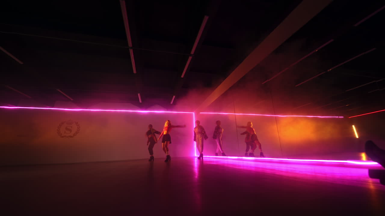 Three girls dancing in the studio. Dancers performing indoors in the pink light. Low angle view.