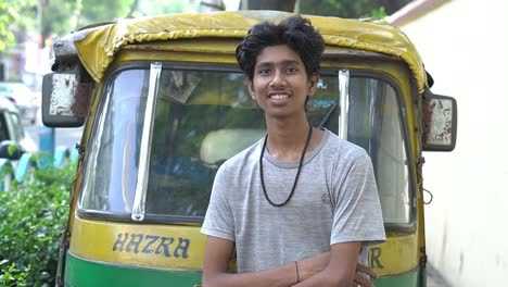 slow motion cinematic shot of a indian auto driver in grey t-shirt standing in side of the road in front of the auto and giving a smile