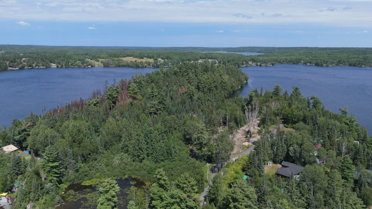 Scenic aerial drone footage of a forested island surrounded by calm blue lake water on a clear summer day