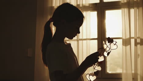 silhouette of a young girl holding heart decorations