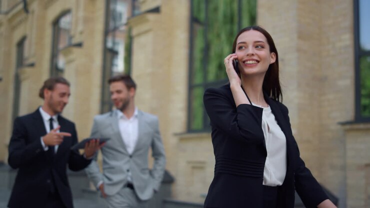 Donna sorridente che usa il cellulare all'aperto. Professionisti che si affrettano al lavoro