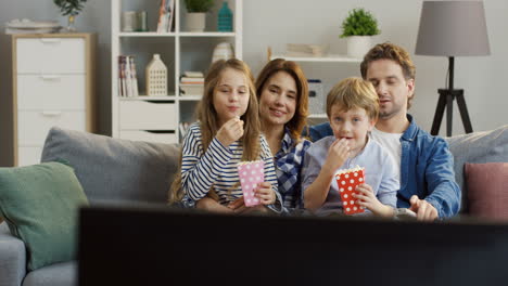 Cheerful-Family-Eating-Popcorn-While-Sitting-On-The-Couch-In-The-Living-Room-And-Watching-Tv