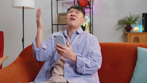 sad asian man use smartphone surprised by bad news fortune loss fail lottery results deadline