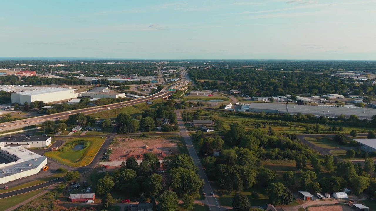 Magazzini industriali si trovano lungo il corridoio dell'autostrada 41, delimitati da alberi fitti, mentre il drone vola all'indietro sopra il paesaggio suburbano nella calda luce del tardo pomeriggio a Neenah, Wisconsin. Ideale per documentari.