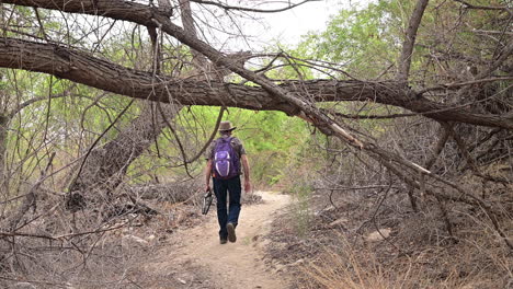 man with backpack and tripod walking in a forest trail on a sunny day