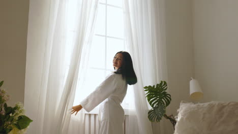 woman opening curtains in a bright bedroom