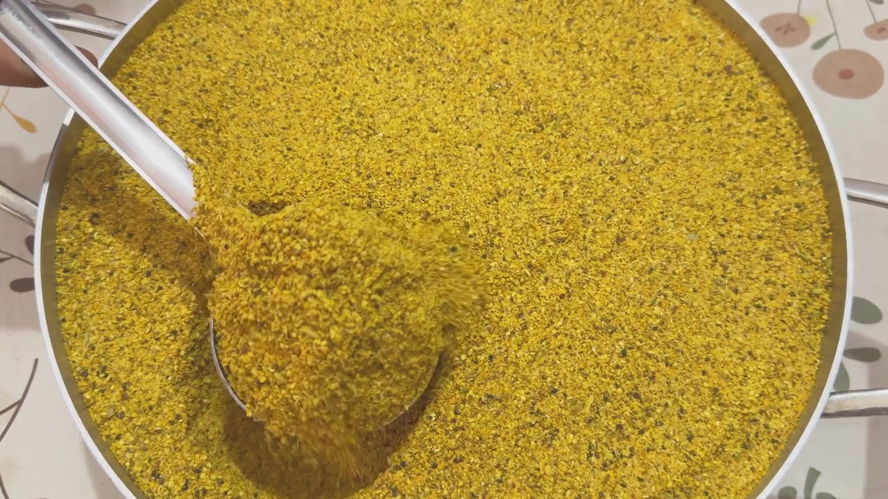 Vista ravvicinata del tradizionale masala indiano di sottaceti di mango che viene prelevato con un mestolo di metallo, rivelando la consistenza grossolana della miscela di spezie di senape e fieno greco utilizzata nella preparazione casalinga dell'achar.