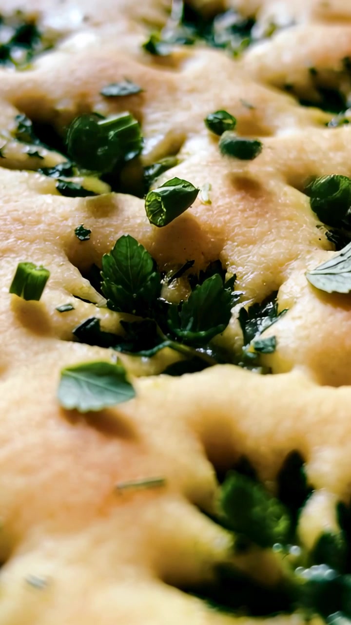 Video verticale: Mano fuori campo che sparge erbe aromatiche verdi su pane con fossette in cucina per insaporire.