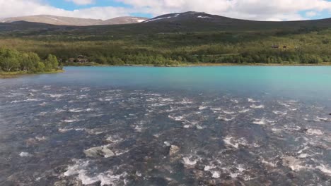 una vista aérea que muestra el prístino desierto de noruega, con un río que fluye, un bosque exuberante y montañas lejanas