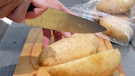 female hands slicing potato into thick cut fries on a wooden chopping board