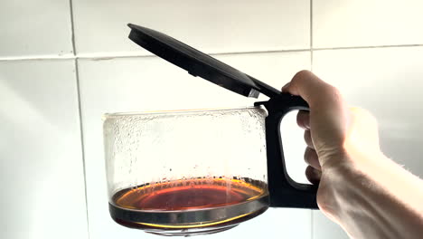 a hand holds a filter coffee pot, opening and closing its lid on a white background