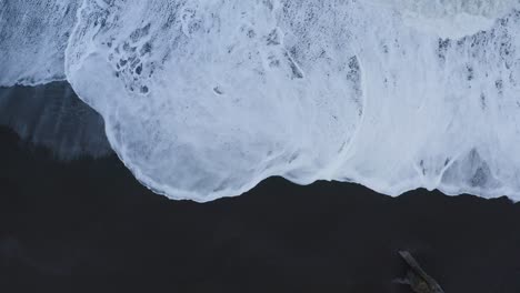 Aerial-top-down-shot-of-foamy-waves-reaching-black-sandy-beach-in-Iceland