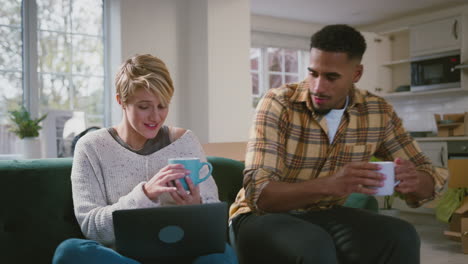 couple unpacking boxes after moving into new home with laptop and hot drinks