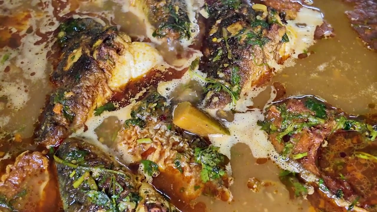 Primer plano de pescado cocinándose en una salsa rica en hierbas.