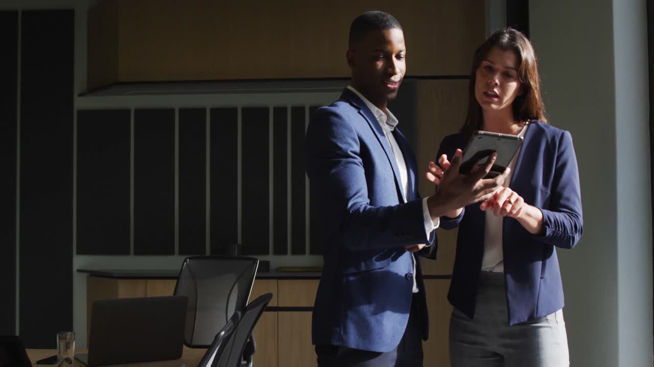 Diverse businessman and businesswoman discussing and using tablet in modern office