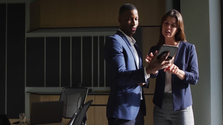 Diverse businessman and businesswoman discussing and using tablet in modern office