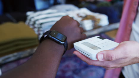 man in clothing store making contactless payment with smart watch at sales desk