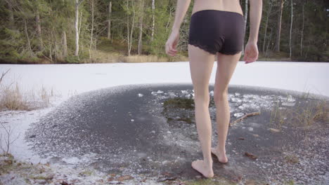 a young woman approaches an ice hole and steps in with one foot