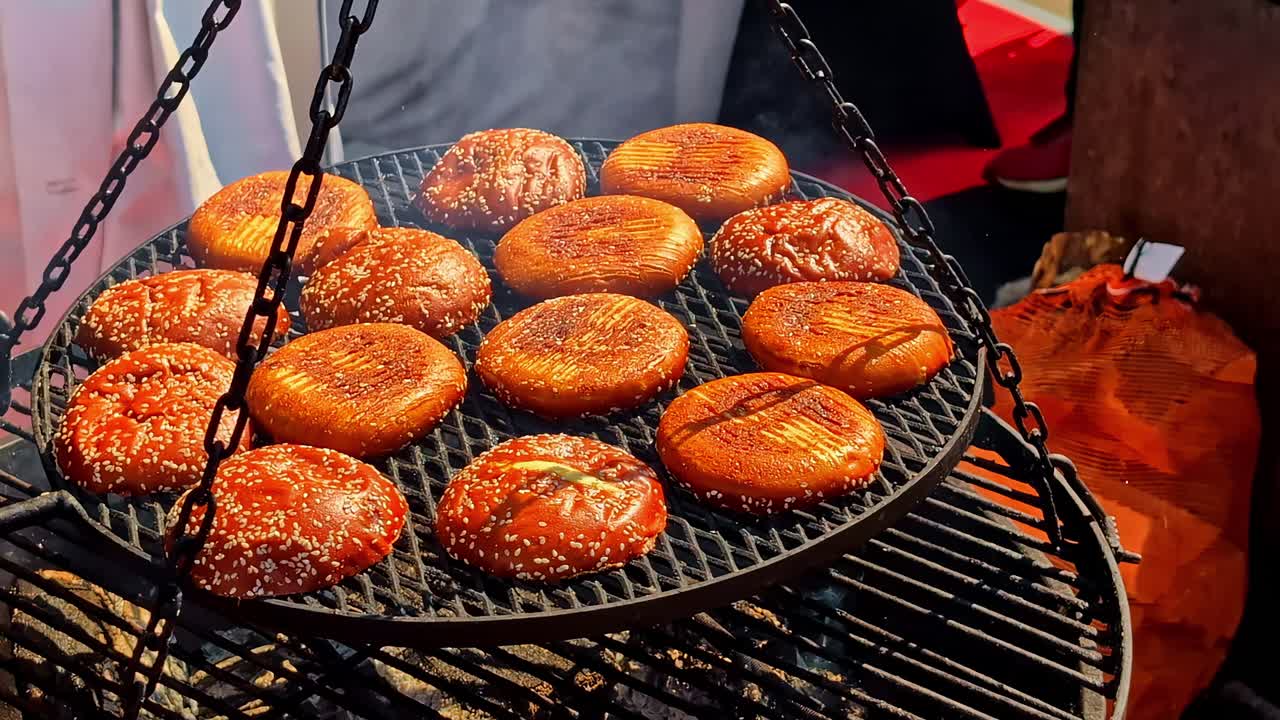 Fresh round buns with sesame seeds toasting on a hanging barbecue grill over open fire, perfect as hamburger buns and capturing rustic street food and artisanal outdoor cooking