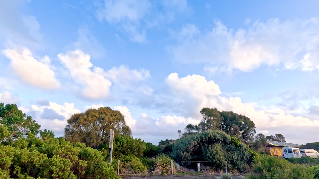 화려한 푸른 하늘 아래의 울창한 초록색과 멀리 떨어진 집들의 조용한 장면, 위대한 바다 도로를 따라 포착되었습니다.