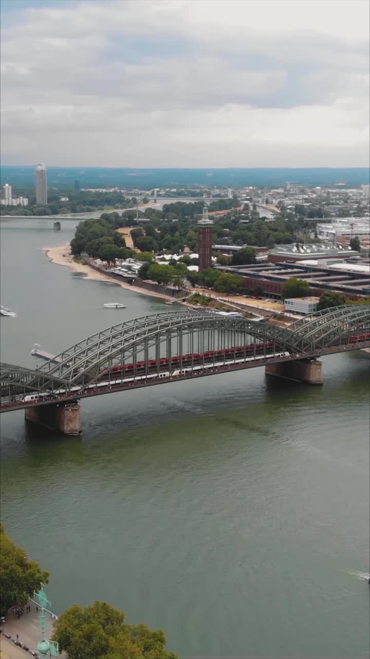 Veduta aerea del Ponte Hohenzollern, un ponte ad arco in acciaio che attraversa il fiume Reno a Colonia, Germania, con traffico ferroviario e pedonale. Video verticale