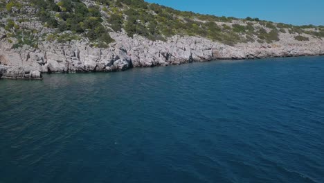Forward-drone-shot-heading-slowly-to-a-rocky-shore-over-the-aegean-sea,-Greece