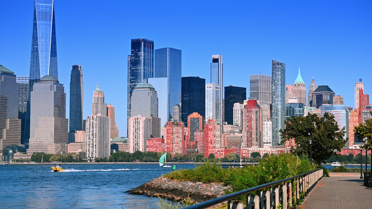 Walk by the beautiful pier in Jersey. Boats sail by the blue waterscape of the Hudson River. Manhattan skyline at backdrop