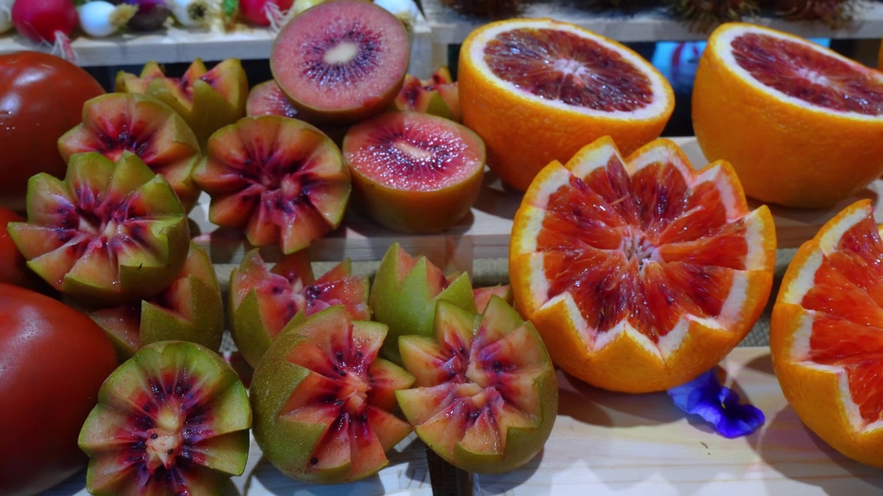 Utskårne kiwi- og blodappelsinhalvdeler arrangert på en fruktutstilling. Nærbilde av dekorativ stjerneformet frukt med rødt og grønt fruktkjøtt på en trekasse.