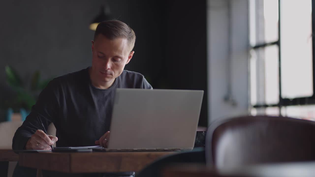 A serious man is a business student working studying sitting at a table and typing a message on a laptop. Typing text on the keyboard
