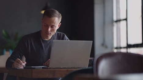 un hombre serio es un estudiante de negocios trabajando estudiando sentado en una mesa y escribiendo un mensaje en una computadora portátil. escribiendo texto en el teclado