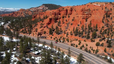 Tracking-Drone-Shot-of-Red-Car-Vehicle-on-Scenic-Route-in-Landscape-of-Utah-USA-on-Sunny-Winter-Day