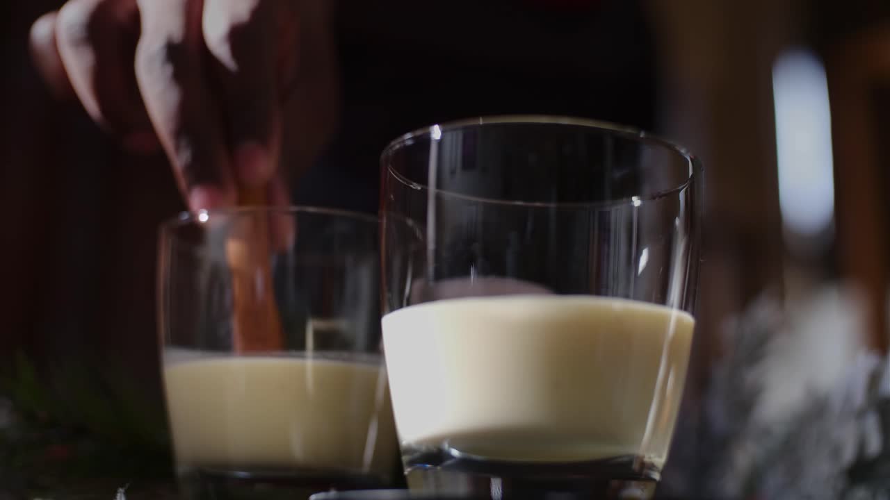 Afrikalı-Amerikalı bir adamın elinin, iki Noel eggnog içeceğine tarçın çubukları koyduğu önden görünüm çekimi.