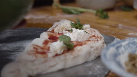 Chef-tops-Neapolitan-pizza-with-basil-leaves-and-olive-oil,-on-wooden-table