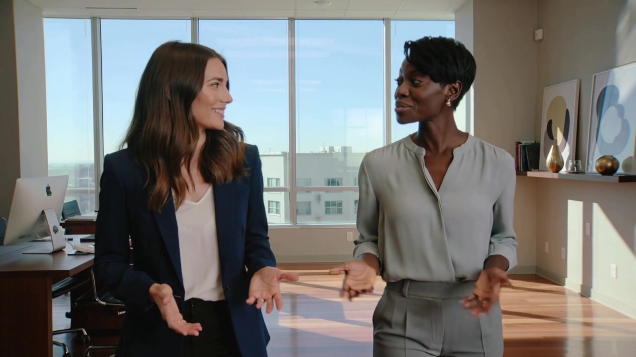 Walking two women in business clothes greeting, discussing plan in sunlit office with tall windows