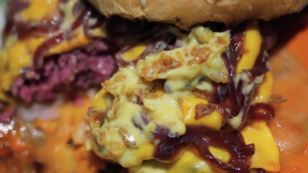 Close up of a loaded burger with melted cheese, caramelised onions, and a creamy sauce on a toasted bun