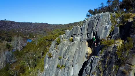 Stationary-hovering-drone-footage-of-an-adult-male-rock-climbing-with-a-scenic-creek-and-mountain-in-the-background