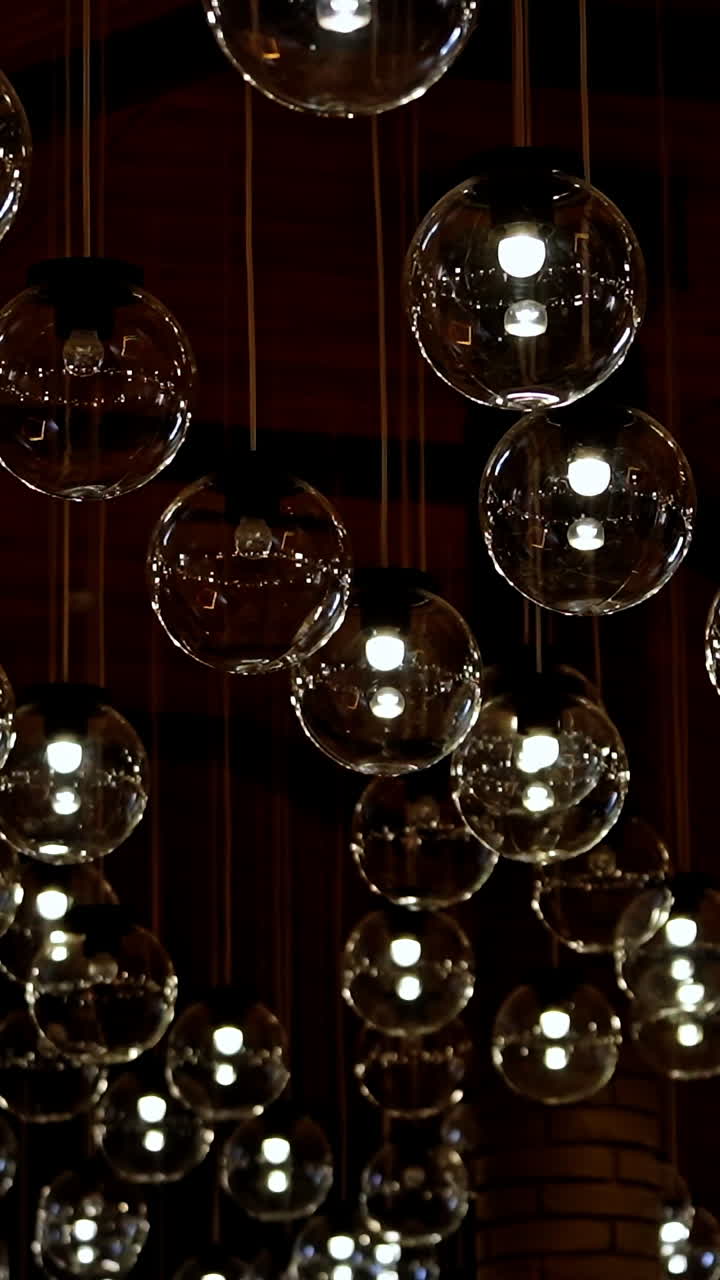 Many light bulbs lighting up. Dark background with lamps becomes bright. Beautiful ceiling with round glass lamps switches on. Vertical video