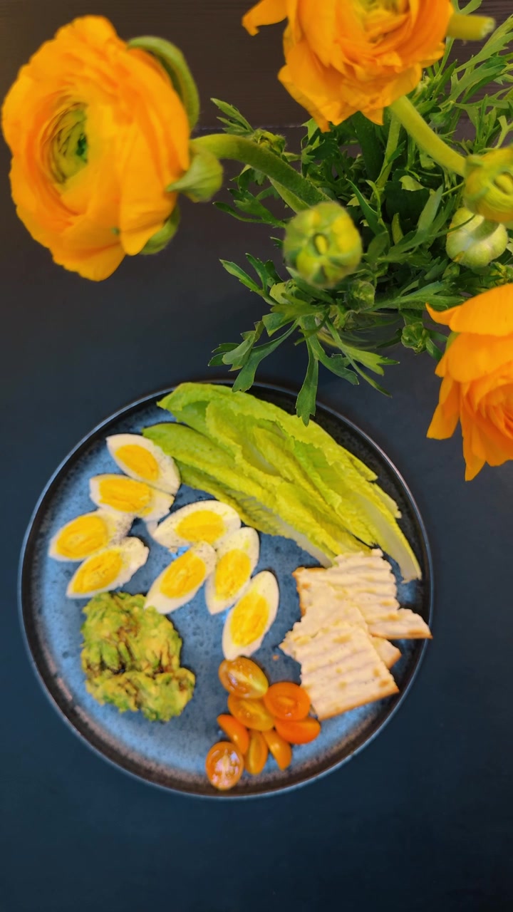 Plato de desayuno saludable con huevos, aguacate y galletas saladas. Vista superior de un plato de cerámica azul con huevos en rodajas, guacamole, lechuga, tomates cherry y galletas saladas.