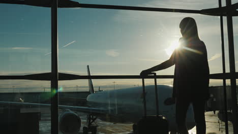 Business-Woman-With-A-Travel-Bag-Somtrit-The-Window-On-The-Airliners-Stands-In-The-Airport-Terminal-