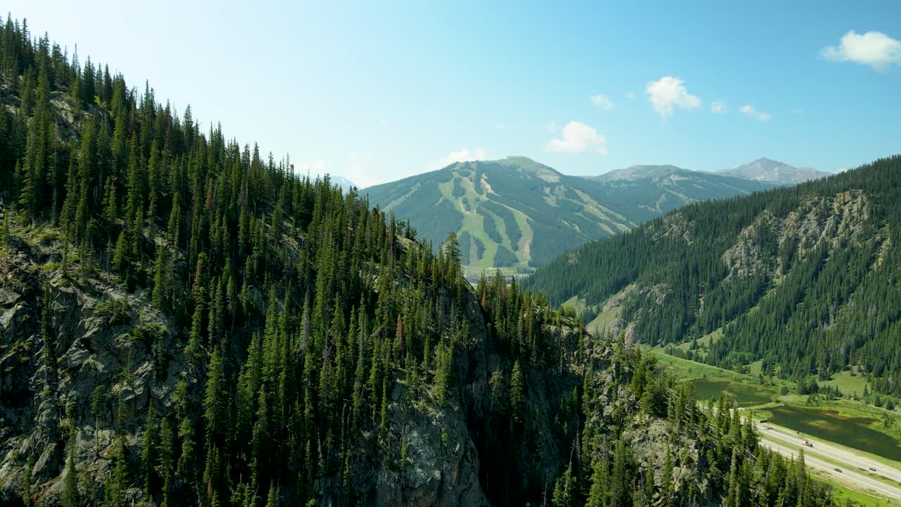 Flying just over a mountain peak and pine trees to reveal Copper Mountain Ski Resort in Colorado