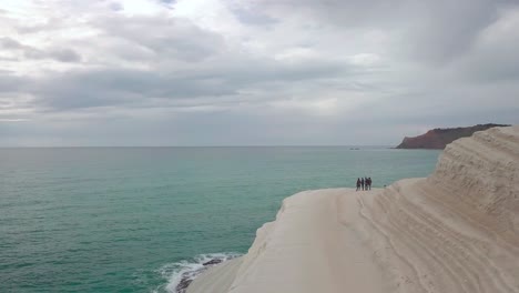 Aerial-footage-boom-out-and-pan-left-of-group-of-friends-admiring-the-views-from-the-white-rock-called-Scala-dei-Turchi,-Stairs-of-the-Turkmen-in-Sicily,-Italy