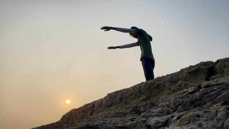Giovane uomo si esercita all'aperto in cima a una collina rocciosa, al tramonto, statico, slow motion.