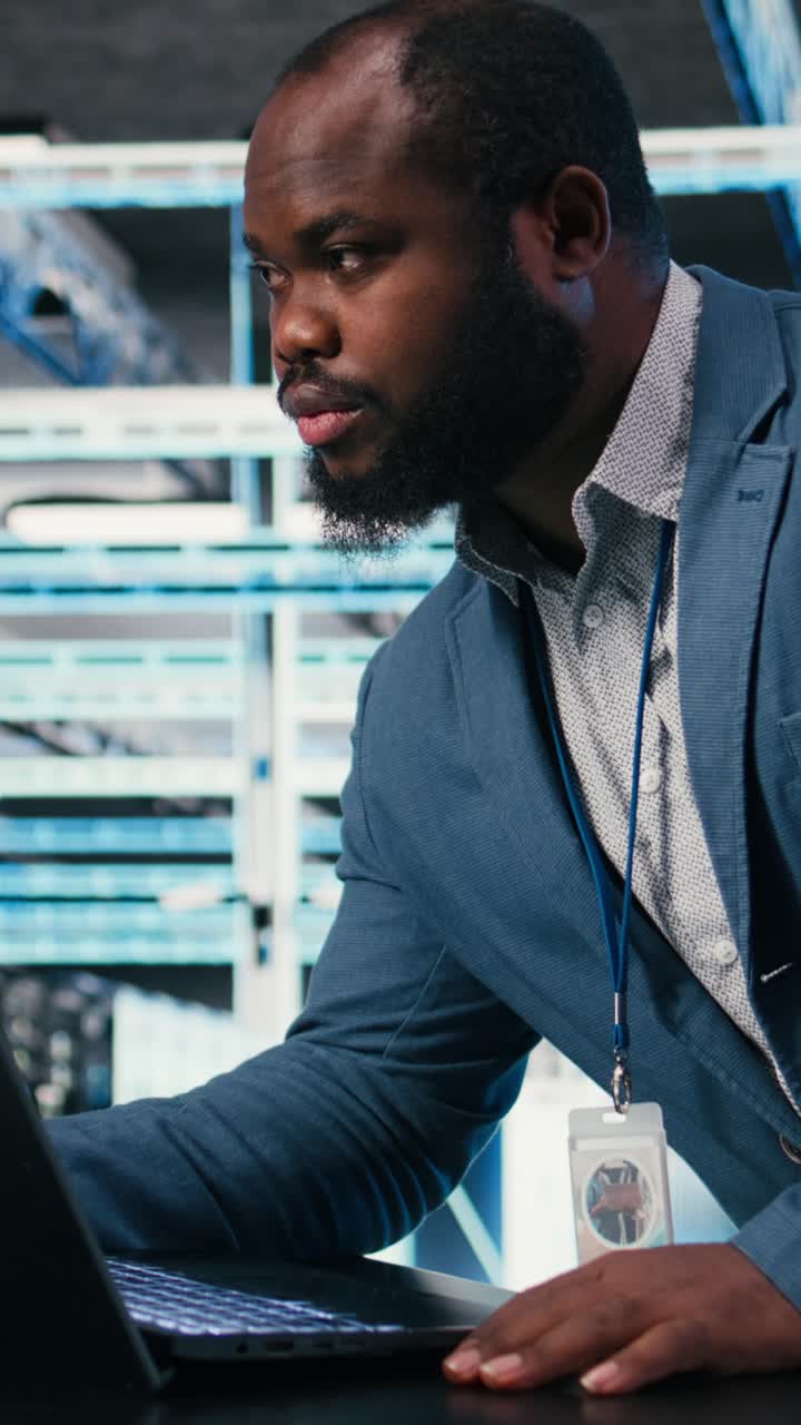 Vertical video Programmer at server farm workplace desk using laptop, doing network management